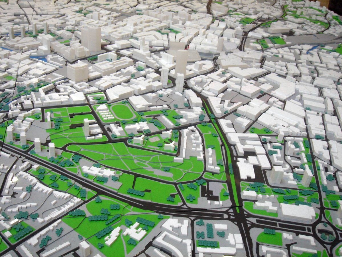 3D model of a city, with buildings represented by white plastic cubes, parks in green fabric, roads in black lines