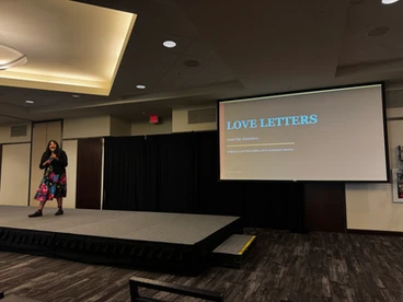 A photo of a speaker with a presentation in the background that reads, "Love Letters"